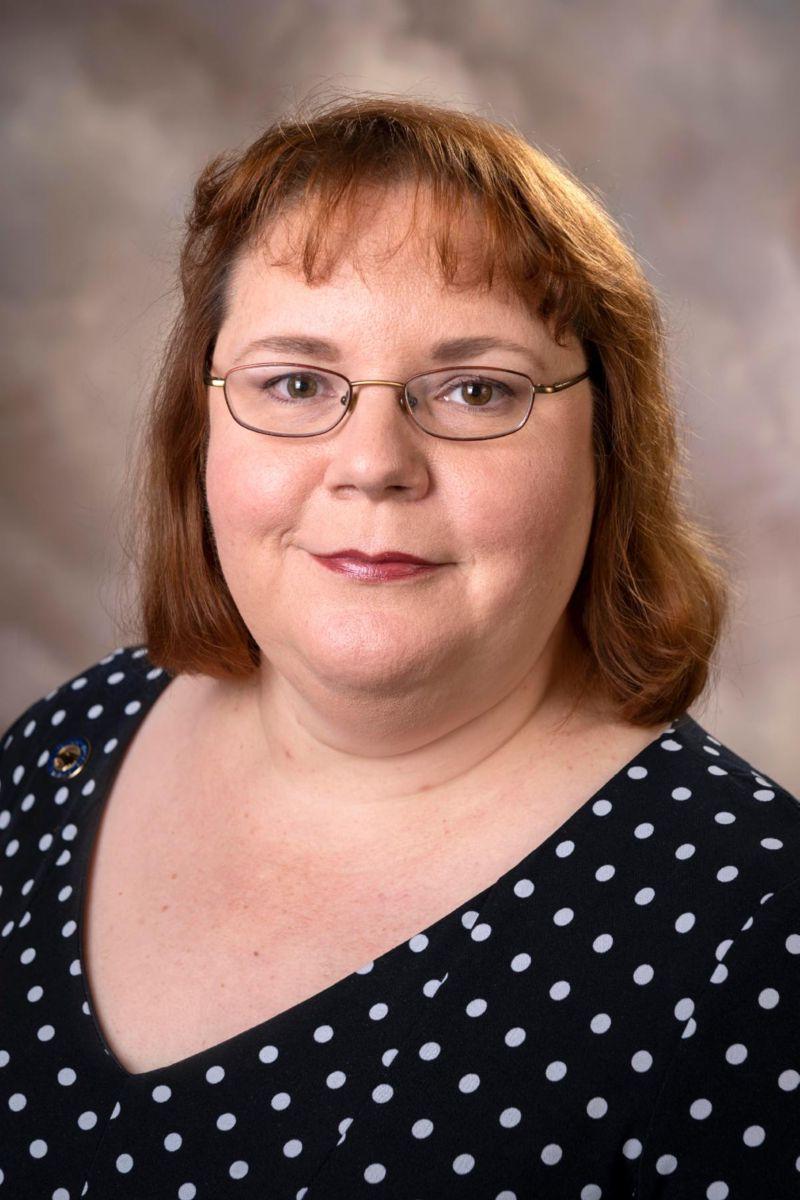 Mrs. Cheryl Ciucevich, a Caucasian female with shoulder length red hair, smiles wearing a black and white polka dot dress.